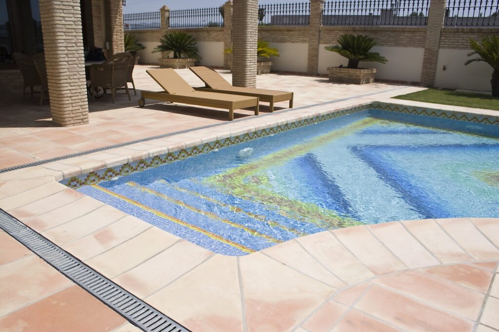 CORONACIÓN PISCINA 50X25 CM. ALREDEDOR BALDOSA MANUAL DE BARRO COCIDO 40X40 CM. COLUMNAS DE LADRILLO 25X12X3 CM.